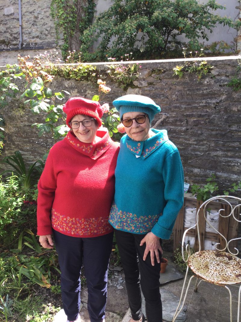 Deux femmes avec chacune un pull et un beret en laine, l'une tout en rouge l'autre tout en bleu.
