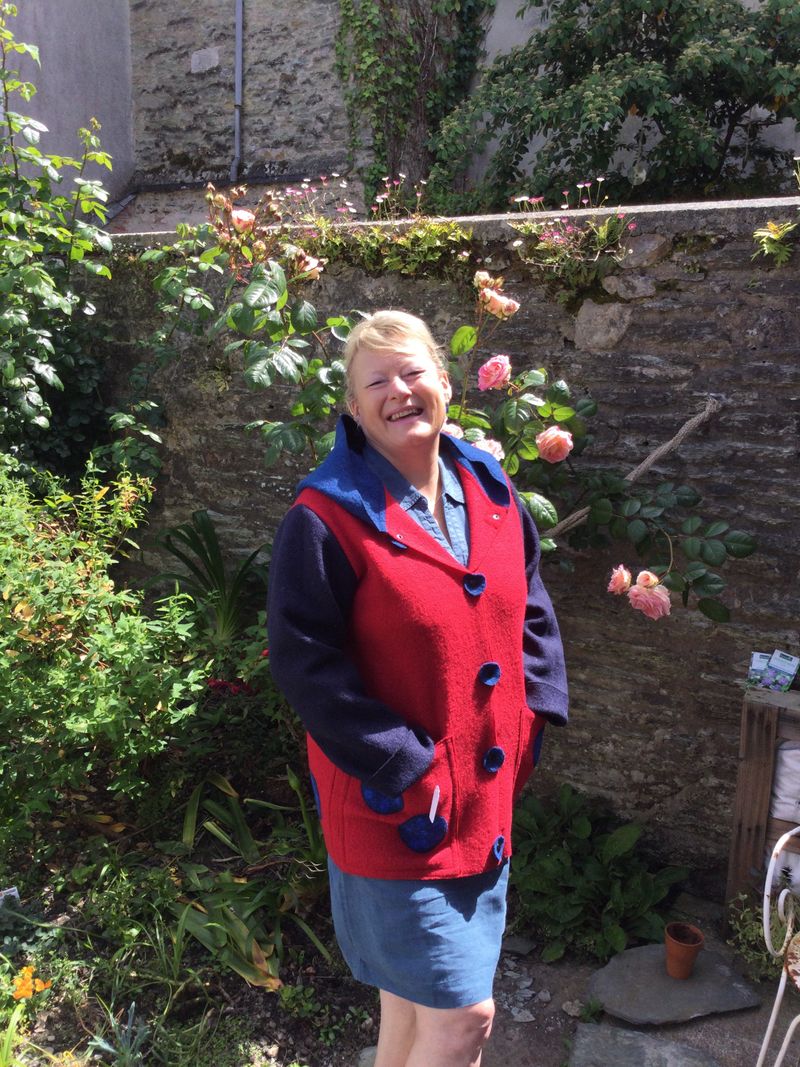 Un femme blonde souriante au soleil avec un manteau rouge et bleue en laine feutré